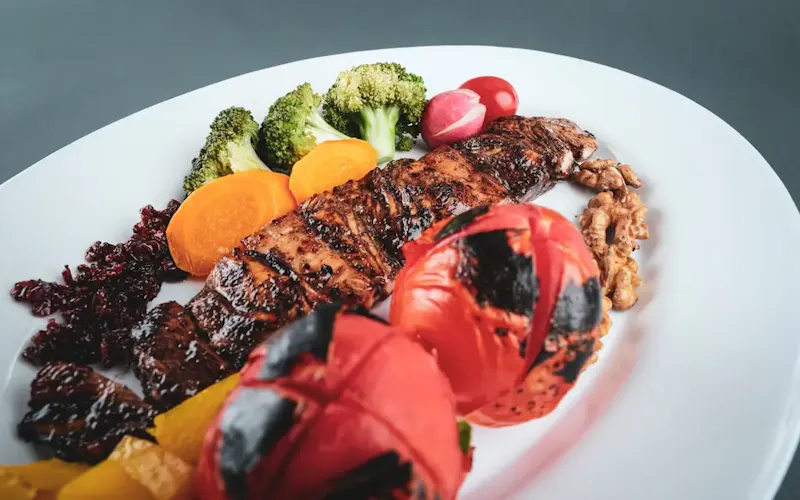 Fotografía de Boucherie Calevoet grilled meat with sliced tomato and green vegetable on white ceramic plate | Foto de Sam Moghadam, en https://unsplash.com/@sammoghadam?utm_source=centralapp&utm_medium=referral