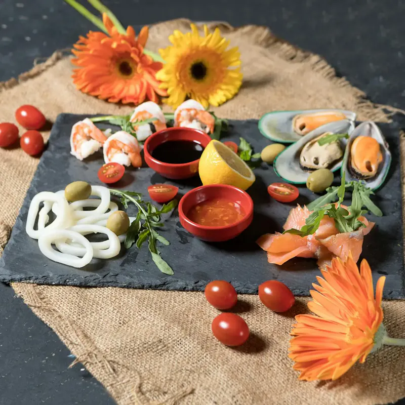 A beautifully arranged seafood platter with flowers and garnishes on a rustic slate. | Photo by Farhad Ibrahimzade, on https://www.pexels.com/@farhad?utm_source=centralapp&utm_medium=referral