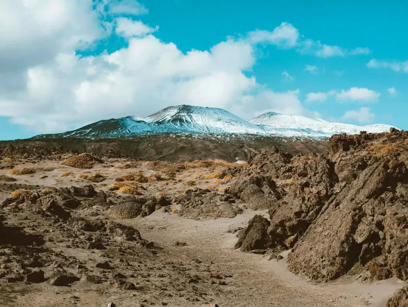Picturesque view of distant mountains with snow on slopes surrounded by rocky terrain under cloud sky | Photo de ROMAN ODINTSOV, sur https://www.pexels.com/@roman-odintsov?utm_source=centralapp&utm_medium=referral