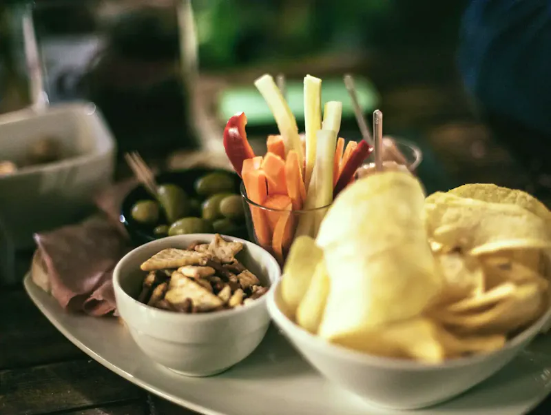 A tempting snack platter featuring crisps, vegetables, and olives, perfect for a casual gathering. | Immagine di SplitShire, su https://www.pexels.com/@splitshire?utm_source=CentralApp&utm_medium=referral