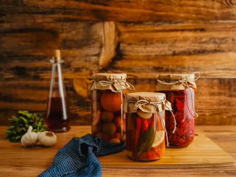 Jars of preserved vegetables on a wooden surface with a rustic background. | Immagine di hello aesthe, su https://www.pexels.com/@helloaesthe?utm_source=centralapp&utm_medium=referral