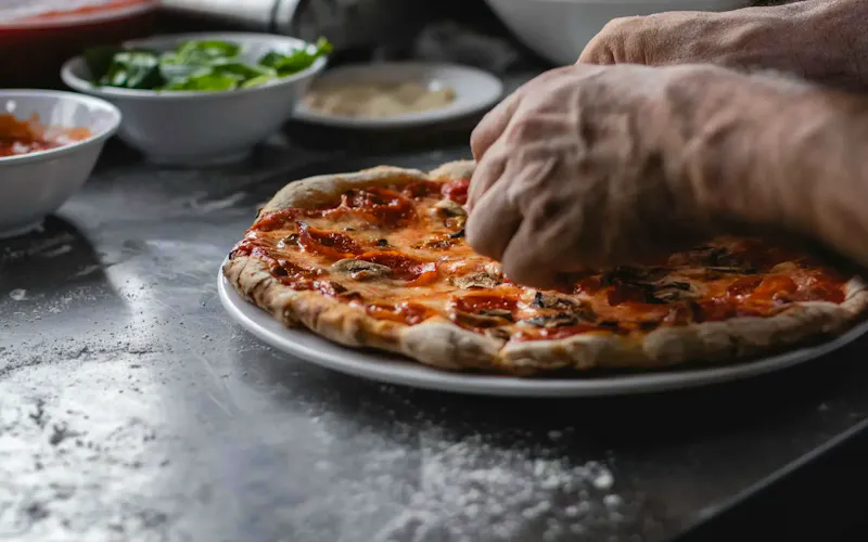 Image of Pizzeria Friggitoria zero81 Close-up of man's hands preparing a freshly cooked pizza with toppings in the kitchen. | Photo by Rodolfo Quirós, on https://www.pexels.com/@rquiros?utm_source=centralapp&utm_medium=referral
