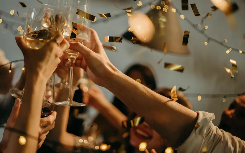 A lively indoor party scene with people toasting champagne glasses amid confetti and warm lights. | Photo by cottonbro studio, on https://www.pexels.com/@cottonbro?utm_source=centralapp&utm_medium=referral