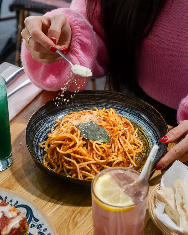 Gros plan d'une assiette de spaghettis bolognese, avec une feuille de basilic chez Ti Amo, avec du parmesan saupoudré à la cuillère.